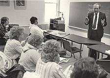 A man in a classroom lecturing in front of a blackboard